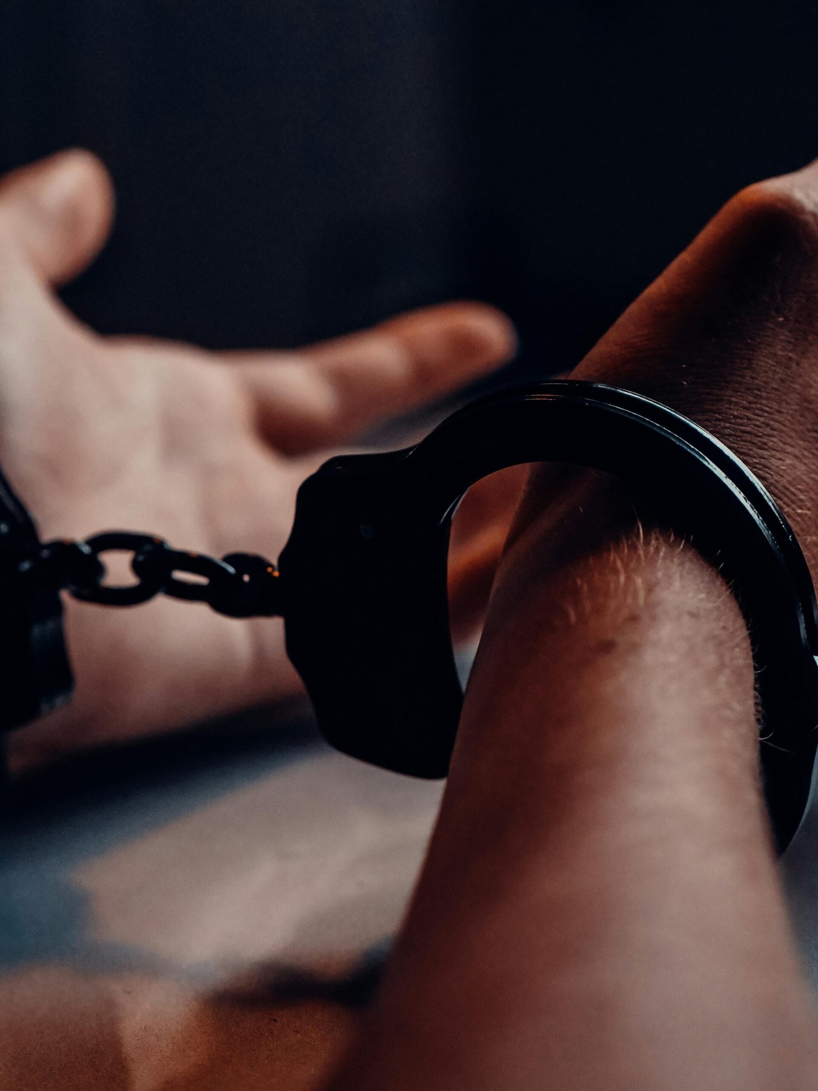 A close-up of human hands handcuffed on a table with a dark background, depicting law enforcement themes.